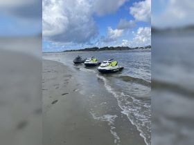 Three jet skis are lined up on the sandy shore, ready for an exciting day on the water. Perfect for adventure seekers looking to explore the coastline.