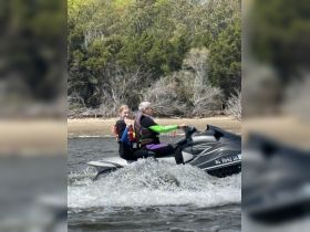 A joyful ride on a jet ski captures the excitement of on-water activities, showcasing a fun moment between a child and an adult in a scenic setting.