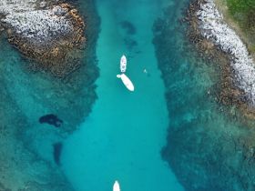 Aerial view of a serene waterway with boats and swimmers enjoying the clear turquoise waters, showcasing a perfect day for aquatic adventures.