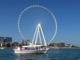A scenic view of a boat cruising near a stunning ferris wheel, showcasing the vibrant cityscape — perfect for capturing the essence of a day on the water.