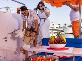 A joyful family moment aboard a boat, with a child being helped by an adult while a vibrant fruit platter is displayed — perfect for family outings and celebrations on the water.