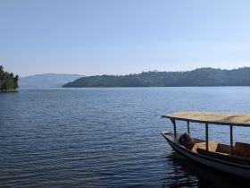 A serene view of a boat docked by the tranquil waters of a lake, surrounded by lush greenery and distant hills, perfect for peaceful getaways.