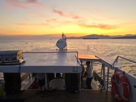 A stunning sunset view from the deck of a boat, with crew members visible, creating a perfect backdrop for memorable evening cruises.