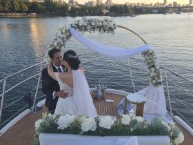 A couple shares a romantic moment during their wedding ceremony on a boat, surrounded by beautiful floral decorations and a stunning waterfront backdrop.