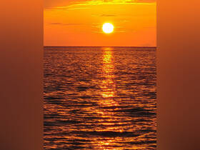 A breathtaking sunset casts a golden glow over the ocean, creating a serene and picturesque scene perfect for romantic evenings or tranquil boat rides.