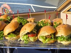 A delicious spread of gourmet burgers garnished with fresh lettuce and herbs, perfect for onboard catering during a boat trip.
