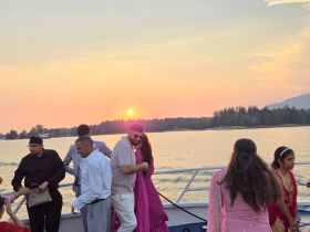 A vibrant group enjoys a sunset celebration aboard a boat, showcasing festive attire and joyful moments against a stunning backdrop.