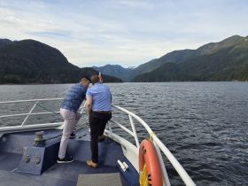 Two individuals enjoy the scenic views from the bow of a boat, surrounded by stunning mountains and tranquil waters — a perfect moment for adventure and exploration.