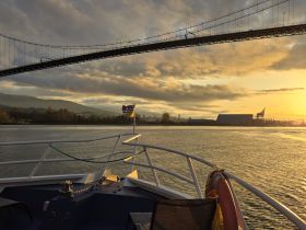 A serene sunset view from the bow of a boat, showcasing the beautiful landscape and a bridge in the background — perfect for tranquil evening cruises.