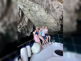 A cheerful group poses on the bow of a boat inside a stunning cave, capturing a memorable moment during their adventure on the water.