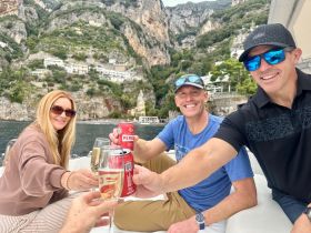 A cheerful group toasts with drinks aboard a boat, surrounded by stunning coastal scenery — perfect for memorable celebrations on the water.