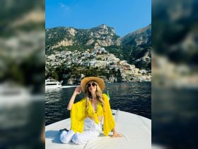 A woman poses on the deck of a yacht with the stunning backdrop of Positano's colorful cliffside homes, capturing the essence of a luxurious coastal getaway.