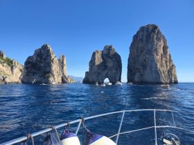 A stunning view of iconic rock formations with several boats navigating the clear blue waters, showcasing the beauty of the coastline.