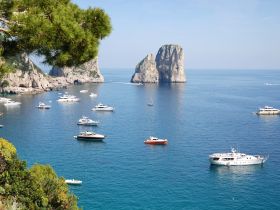 A stunning view of multiple yachts anchored in a picturesque harbor, framed by dramatic cliffs and clear blue waters — a perfect destination for luxury boating adventures.