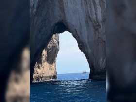A stunning view of a natural rock arch with a boat passing through the vibrant blue ocean, showcasing the beauty of coastal landmarks.