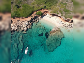 An aerial view of a stunning coastline with crystal-clear turquoise waters and a boat anchored near a secluded beach — a perfect spot for relaxation and exploration.