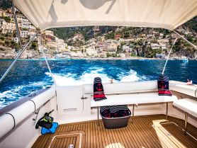 A stylish interior view of a boat showcasing comfortable seating and a scenic backdrop of coastal cliffs, perfect for relaxing while cruising.