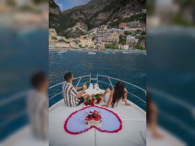 A couple enjoys a romantic moment on a boat in Positano, surrounded by beautiful scenery and a heart-shaped arrangement of roses, perfect for celebrations or proposals.