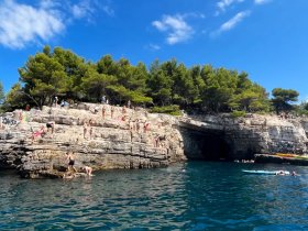 A vibrant scene of people enjoying cliff diving and swimming in clear waters, surrounded by stunning rocky cliffs and lush greenery — a perfect summer adventure.