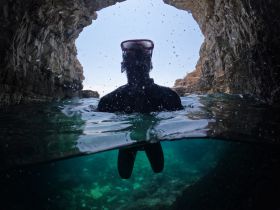 A snorkeler explores a stunning underwater cave, capturing the thrill of adventure in crystal-clear waters — a perfect highlight for underwater excursions.