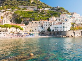 A stunning view of the Amalfi Coast, showcasing picturesque white buildings nestled against lush green hills and crystal-clear waters — a perfect destination for scenic boat tours.