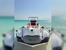 A sleek speedboat rests on the sandy shore, showcasing its stylish design against the backdrop of clear turquoise waters — perfect for a day of adventure on the sea.