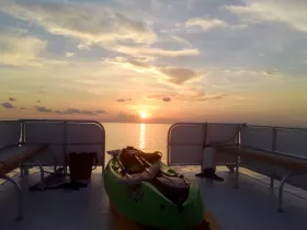 A serene view from the interior of a boat featuring a kayak and a stunning sunset over calm waters, perfect for relaxing moments on the water.