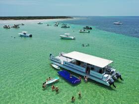 A vibrant scene at a sandbar with guests enjoying paddleboarding and swimming around a boat, perfect for a fun day on the water with friends and family.