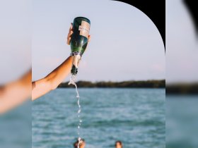 A hand joyfully pours champagne into the air, capturing the essence of celebration on the water — perfect for party vibes and memorable moments.