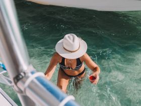 A woman enjoys a refreshing cocktail while wading in crystal-clear waters, capturing the essence of a perfect beach day on a boat trip.