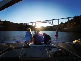 A group enjoys a picturesque sunset on a boat, with a stunning bridge in the background — a perfect moment for relaxation and scenic views on the water.