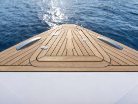 A close-up view of the bow of a sleek boat, showcasing the elegant wooden deck and the shimmering water in the background — perfect for showcasing luxury boating experiences.