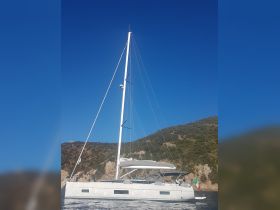 A stunning side view of a sleek sailboat navigating through clear waters, set against a backdrop of lush hills — perfect for sailing enthusiasts and charter adventures.