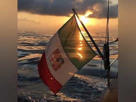 A stunning sunset view featuring the Italian flag fluttering on a sailboat, capturing the serene beauty of sailing on calm waters.