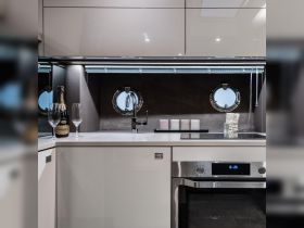 A modern boat kitchen featuring sleek cabinetry, a champagne bottle, and porthole windows, perfect for entertaining guests on board.