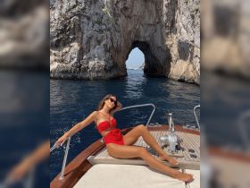 A woman relaxes on the bow of a boat, enjoying the stunning coastal scenery with a natural rock arch in the background — a perfect moment for sunbathing and exploring.