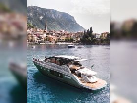 A stunning yacht glides through the serene waters, framed by picturesque mountains and charming lakeside villages, perfect for luxury cruising.