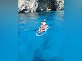 Two friends enjoy paddleboarding in crystal-clear waters near a stunning cave, capturing the essence of adventure and fun on the water.
