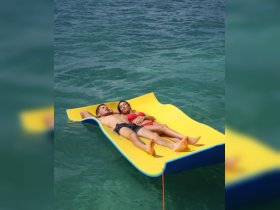 A couple enjoys a relaxing day on a floating mat in clear waters, perfect for sunbathing and unwinding during a summer getaway.