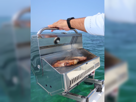 A close-up of a stainless steel grill on a boat, with steaks sizzling on the grill — perfect for onboard barbecues and enjoying delicious meals at sea.