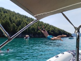 A young man leaps off the side of a boat into the crystal-clear waters, capturing the thrill of summer fun and adventure on the water.