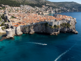 A stunning aerial view of Dubrovnik's historic coastline, showcasing the iconic city walls and vibrant rooftops against the crystal-clear waters — a perfect destination for sightseeing and exploration.