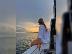 A young woman enjoys a serene sunset view from the deck of a boat, capturing the tranquil beauty of the water and sky.