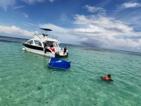 A child swims near a boat in crystal-clear waters, showcasing a fun day on the water with family and friends — perfect for snorkeling and aquatic adventures.