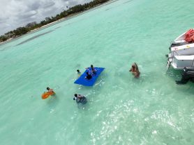A lively group enjoys a fun day in the turquoise waters, featuring floating mats and playful activities — perfect for family outings or beach adventures.