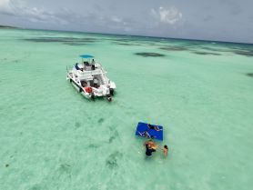A lively group enjoys a fun day on the water, swimming around a boat in shallow turquoise waters — perfect for sandbar stops and family adventures.