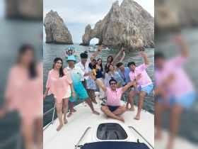 A lively group of friends celebrates on the deck of a boat near the iconic rock formations of Cabo San Lucas, capturing the essence of a fun-filled day on the water.