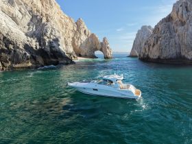 A stunning aerial view of a sleek speedboat navigating through turquoise waters near dramatic rock formations, showcasing the beauty of coastal landscapes.