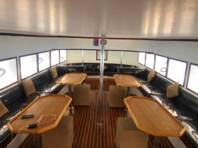 Interior view of a spacious boat cabin featuring comfortable seating and tables, perfect for relaxing and socializing while on the water.