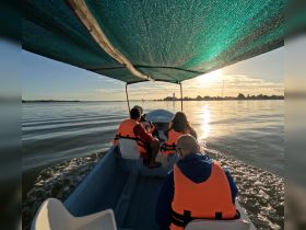A group enjoys a scenic boat ride at sunset, capturing the serene beauty of the water and the vibrant colors of the sky — perfect for memorable outings.